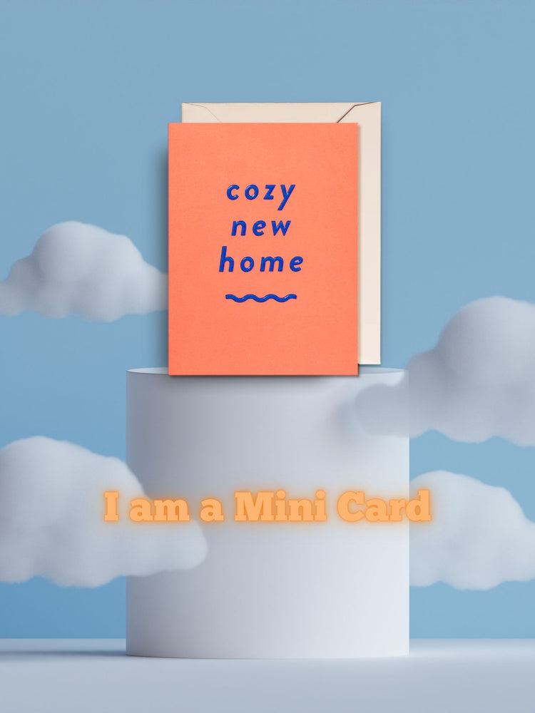 Die Mini-Grußkarte "cozy new home" (Orangefarbener Hintergrund auf blauer Schrift) mit passendem weißen Umschlag veranschaulicht dargestellt.