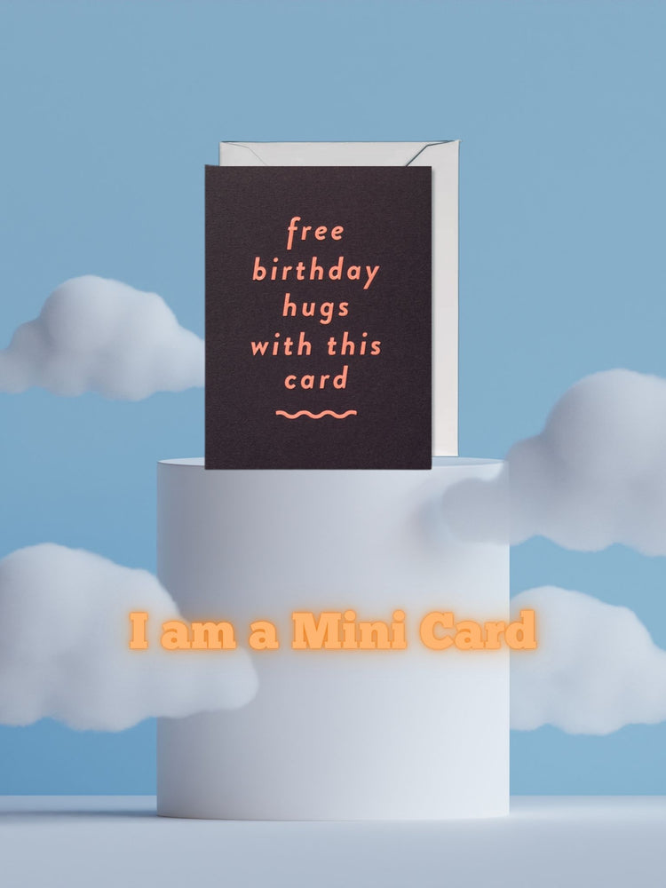 Mini-Grußkarte mit dem Schriftzug "free birthday hugs with this card" von Lagom Design (weinrot/brauner Hintergrund trifft auf Schriftzug in Orange) - Dargestellt auf einem Podest mit Wolken-/Himmel-Hintergrund
